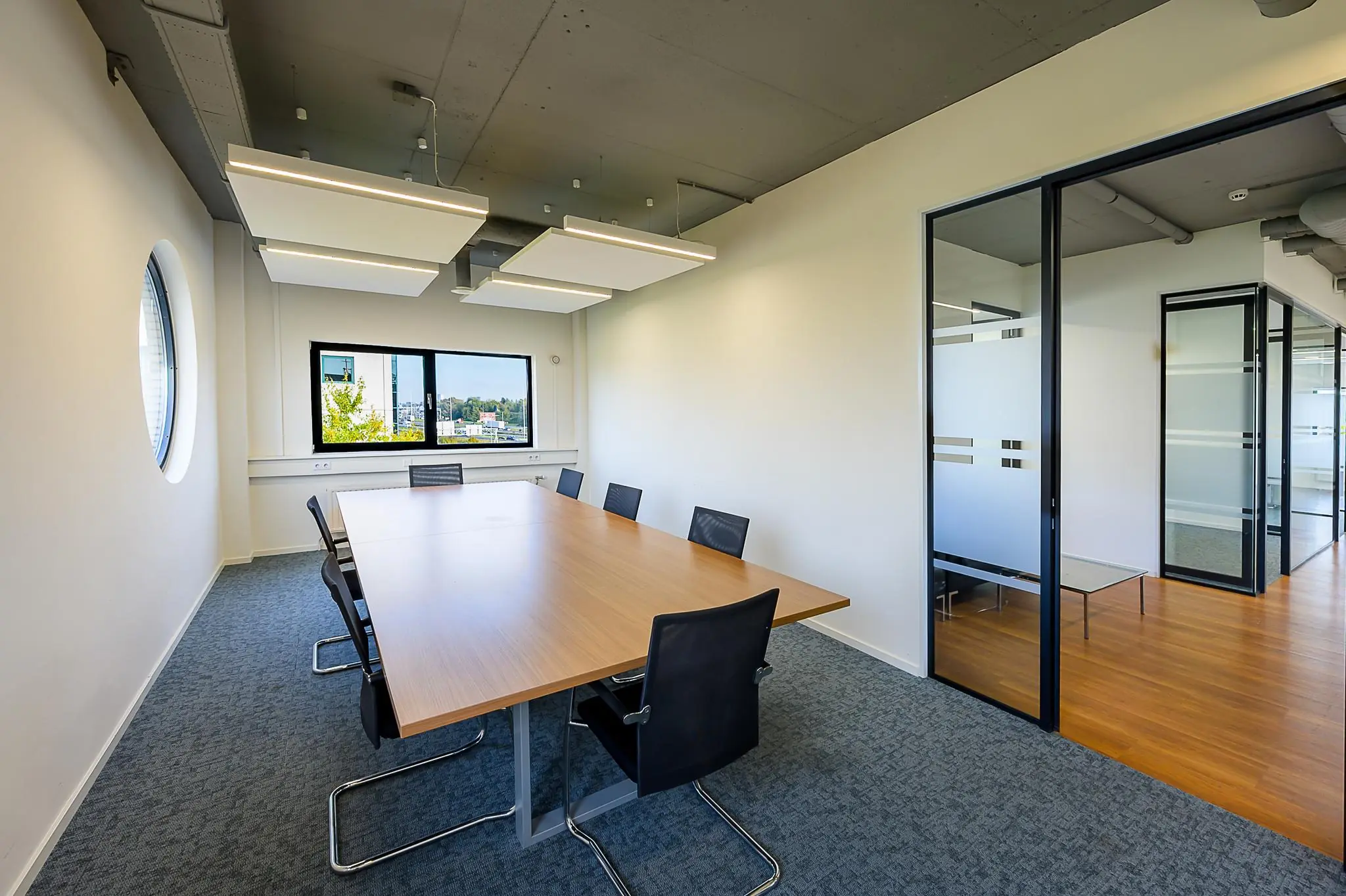 Vergaderruimte aan de K.P. van der Mandelelaan met een grote houten tafel, zwarte stoelen en uitzicht op de stad.